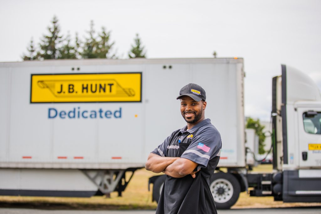 J.B. Hunt dedicated driver stands and smiles in front of a J.B. Hunt DCS trailer.