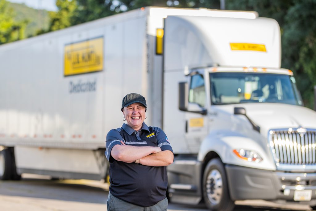 J.B. Hunt driver stands and smiles in front of a day cab and trailer.