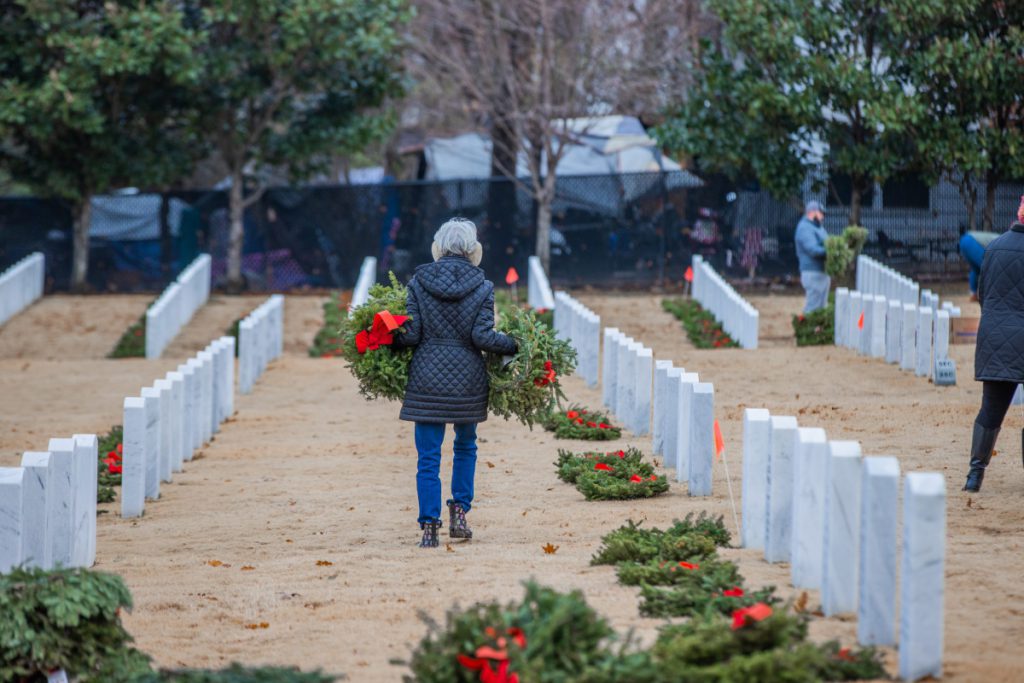 Wreaths Across America volunteer carrying wreaths at a national cemetery.