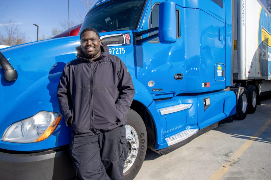 Rhico, owner operator, leans on his truck and smiles.