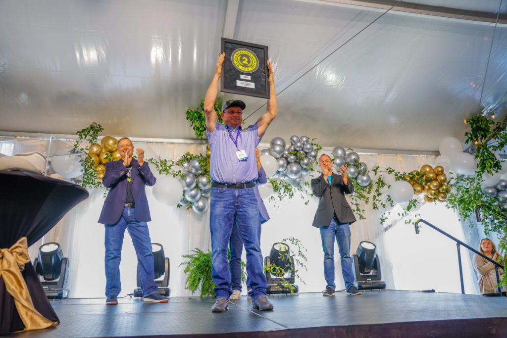 J.B. Hunt's first-ever Final Mile 2 million mile safe driver holds up his award on stage as crowd applauds.