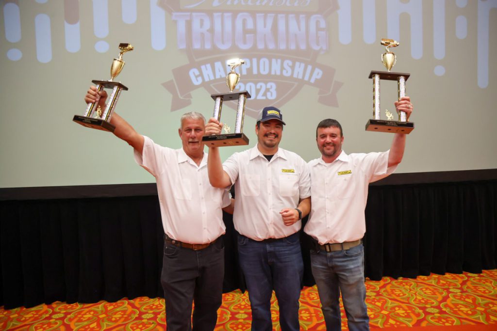 Three J.B. Hunt drivers stand together and lift up their trophies.