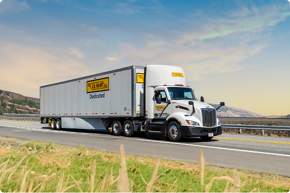 A dedicated contract services truck driving down a rural highway with wheat in the foreground