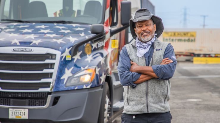 J.B. Hunt veteran driver next to parked truck with an American flag wrap